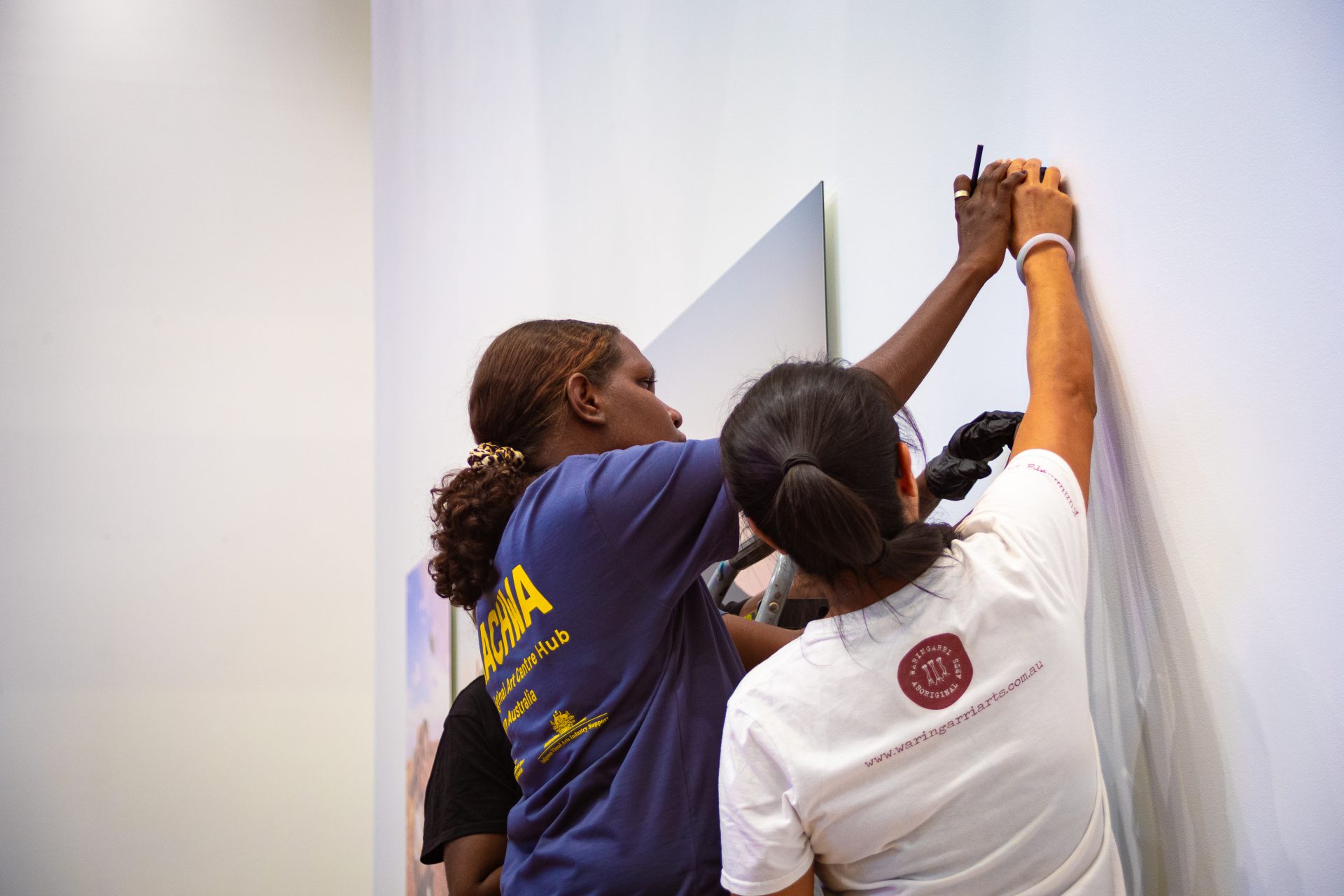 Jade Butler and Jacky Cheng working on installing artworks at the Martumili Gallery as part of Our Future: Aboriginal Arts Worker Training Program, Parnpajinya (Newman), 2023. Photograph by Jess Russell.