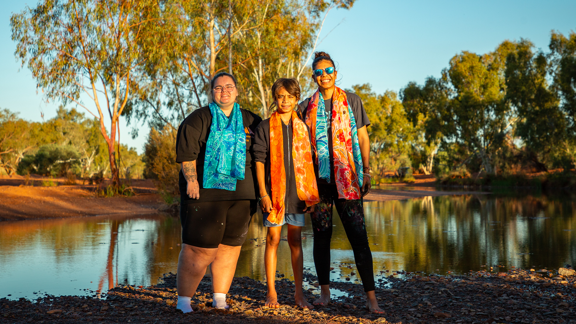 Rekeshia Goodwin (left) and Ruby Djikarra Alderton (right), with their silk painting, Our Future: Aboriginal Arts Worker Training Program at Sandy Creek, Nyiyaparli Country (Newman). Photograph by Jessica Russell.