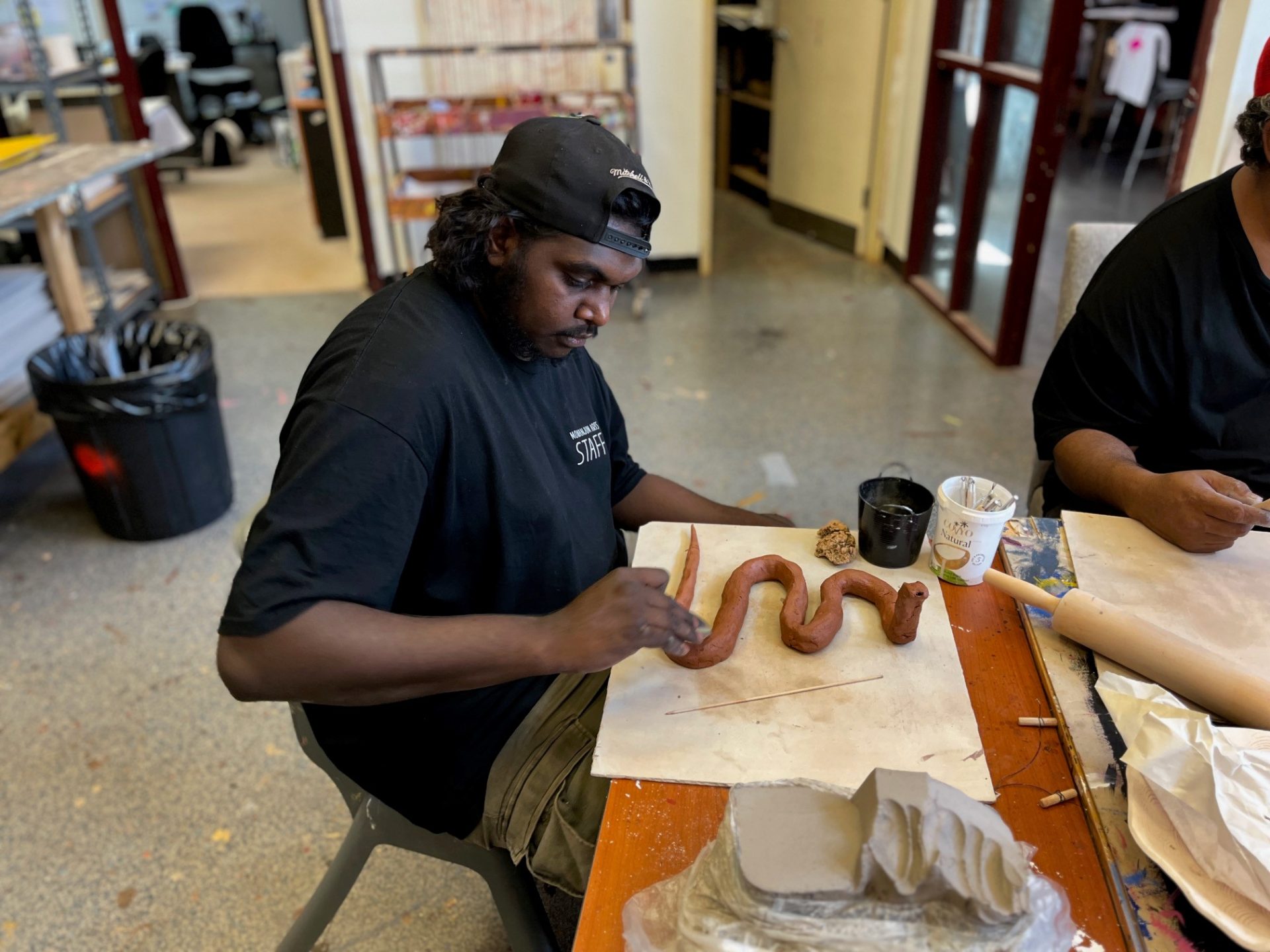 Artist at the Mowanjum Arts and Cultural Centre carefully sculpting and shaping a snake from clay during a workshop facilitated by Tanya Lee and Robyn Lees, Our Country Moves Program, (Derby), 2024. Photo by AACHWA.