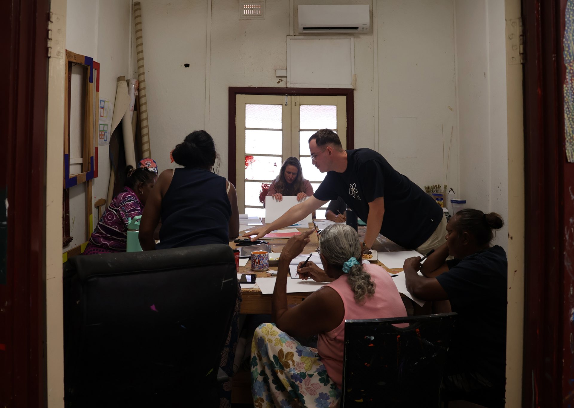Tobie George presenting to Yinjaa-Bari Art’s Justina Willis, Laura Povey, Dawn Sandy, Allery Sandy, Rachael Sandover, Michelle Adams, Renee (Cherine) Wally and Rodney Adams, Our Mob Online brand discovery visit, Leramugadu (Roebourne), 2025, photo: AACHWA
